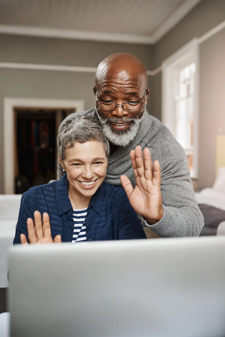Elderly couple waving at family on the other end of the computer