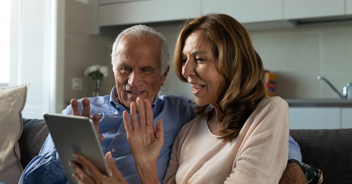 Facetime for Seniors: Senior couple sitting on couch Facetiming with grandchildren on their ipad