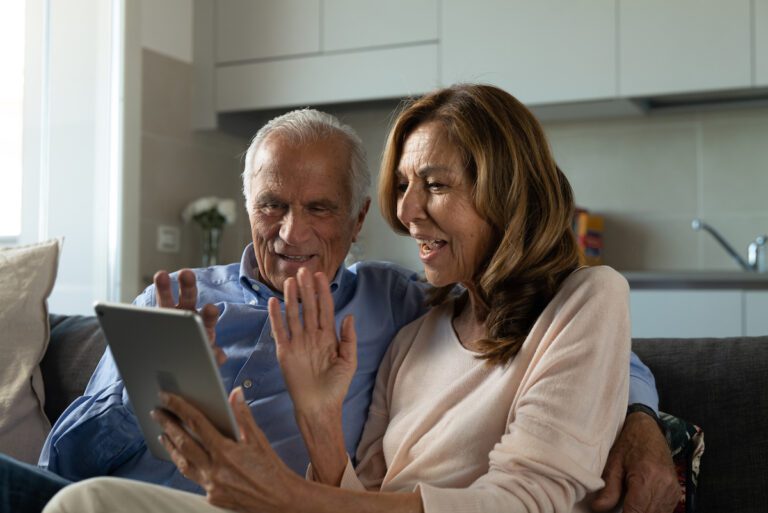 Facetime for Seniors: Senior couple sitting on couch Facetiming with grandchildren on their ipad